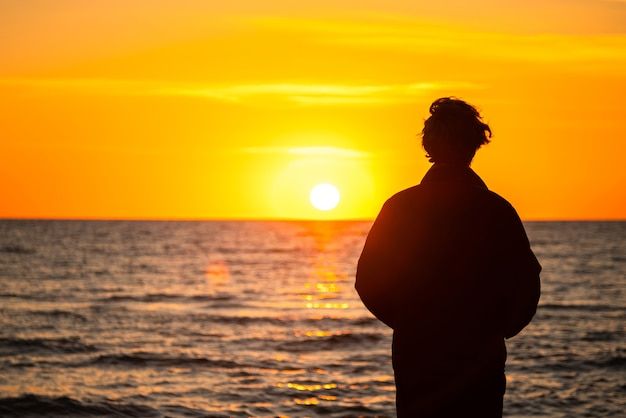 A solitary person looking out over a quiet landscape at sunset, symbolizing reflection, solitude, and emotional acceptance.