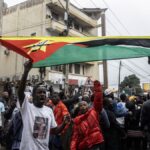 Protesters in Mozambique rally against election results, waving flags and holding signs during a large public demonstration.