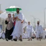 Muslim pilgrims using umbrellas and water bottles to shield themselves from heat in Mecca during Hajj 2025.
