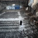 Ruins of a destroyed university building in Gaza, with debris and broken furniture symbolizing scholasticide.